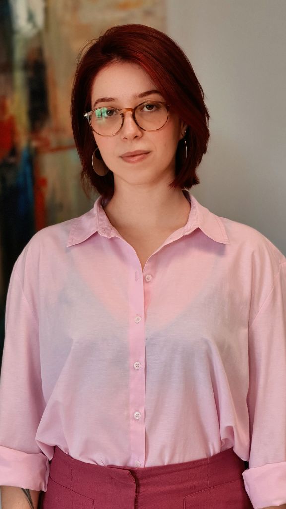 Nadyne em camisa rosa, retrato calmo e frontal.
